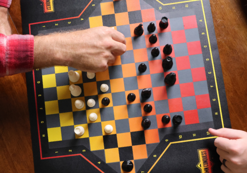 Hands of two players playing strategy board game Crown Conquest witth he board and game pieces visible